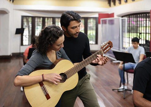 Teacher guiding a female student taking guitar lessons at a music studio - arts and entertainment concepts