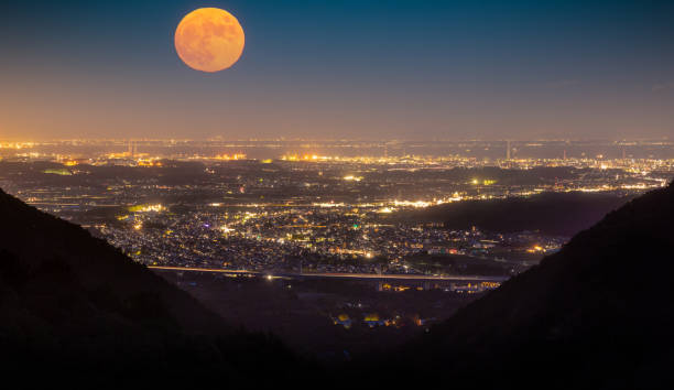 A  full orange moon rises over city. View from high in the mountains.