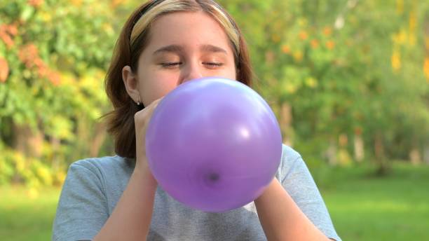 una adolescente infla un globo lila de cerca contra el fondo de la naturaleza - balloon blowing inflating child fotografías e imágenes de stock