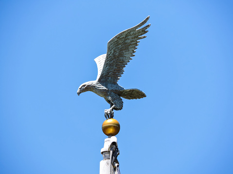 Close up of an eagle sitting on top of a flag pole against a clear blue sky.