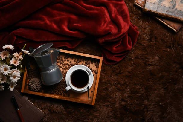 Wooden tray with moka pot, coffee cup and roasted coffee beans on brown carpet.