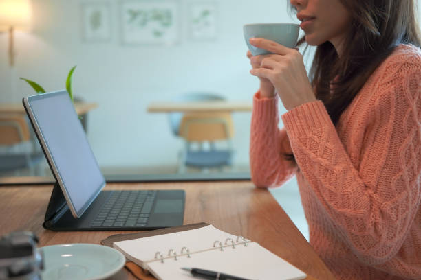 istock Young asian woman in warm sweater drinking hot coffee and using computer tablet at home. 1348175748