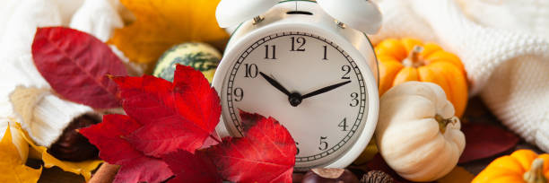 istock Daylight savings and fall time change concept. Autumn composition with retro alarm clock, bright yellow and red leaves, pumpkins, wallnut, cinnamon, anise. Cozy home atmosphere. Banner 1348183721