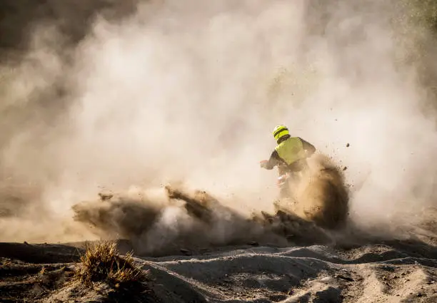 Male motocross rider racing in dust, rear view