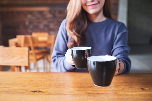 Closeup image of a young woman holding and serving two cups of coffee