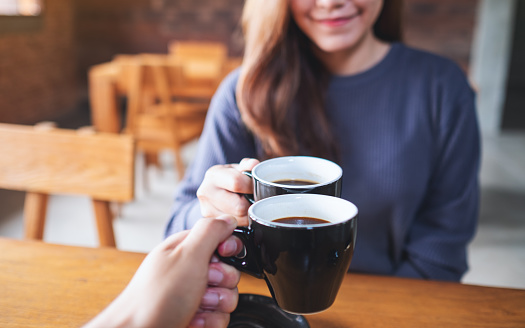A young woman and a man clinking coffee mugs together in cafe