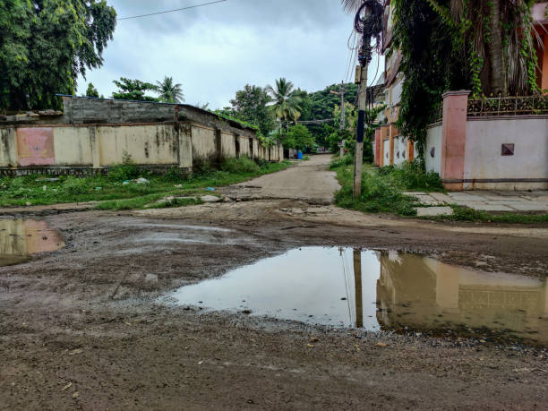 istock grey color road constructed from cement surrounded with Indian styled homes in cloudy climate. Rain water covered the road after heavy rain. Dramatic dark clouds covered the sky. 1348195900