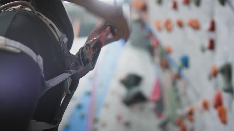 Sport athletic woman secures the safety rope, carabiner hook. Attaches the belay to the carabiner. Climbing solo in indoor gym. Slow motion