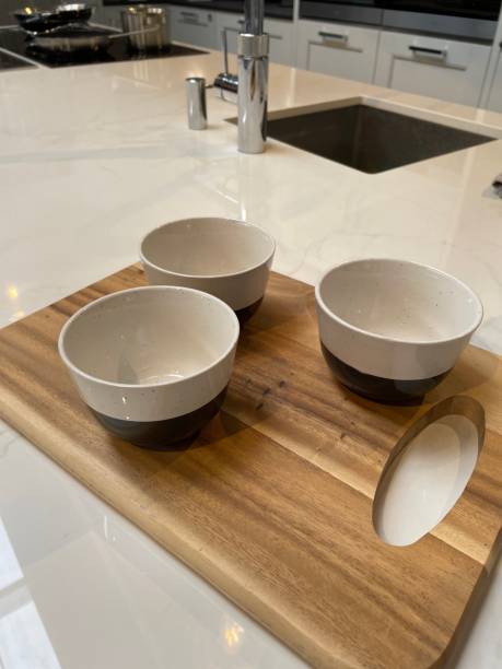 istock Close-up image of modern kitchen design with central island breakfast bar, white composite corian countertop and cereal bowls on wooden chopping board, cabinets, sink and mixer tap background 1348203492