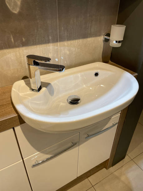istock Image of modern, white luxury bathroom suite with contemporary ceramic sink basin with chrome mixer tap integrated into a wooden counter over a glossy, white vanity unit, tooth brush holder and large beige stone granite wall tiles 1348204728