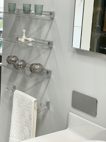 Stock photo of luxury bathroom suite with white ceramic fittings and glass floating shelves displaying glasses.