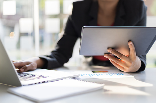 Business man holding tablet working on laptop and analyzing business plan.