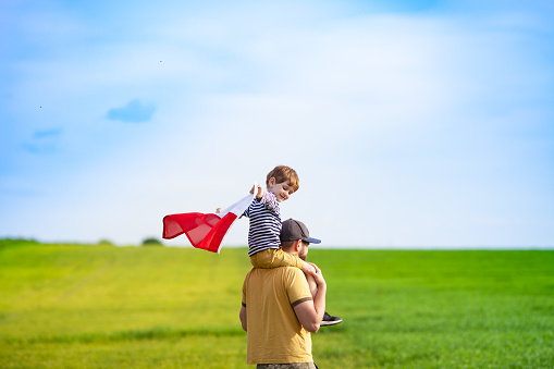 Dad with his little son walking in the field holding flag of Poland. Fathers day in Poland. Polish Flag Day. Independence Day. Love Poland, travel and learn polish language concept.