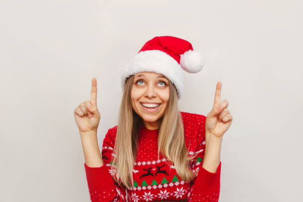 istock A young woman in a red deer sweater and a Santa hat points up at empty copy space. Christmas and New Year concept 1348207832