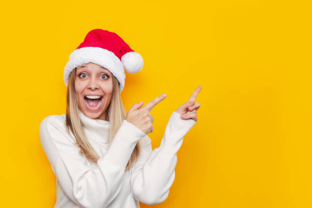 istock A young woman in a white warm sweater and a red Santa hat points at copy space for text or design. Christmas and New Year concept 1348207917