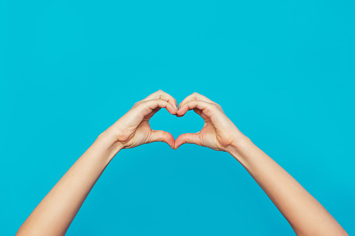 Female hands showing a heart shape isolated on a bright color blue background. Sign of love, harmony, gratitude, charity. Feelings and emotions concept