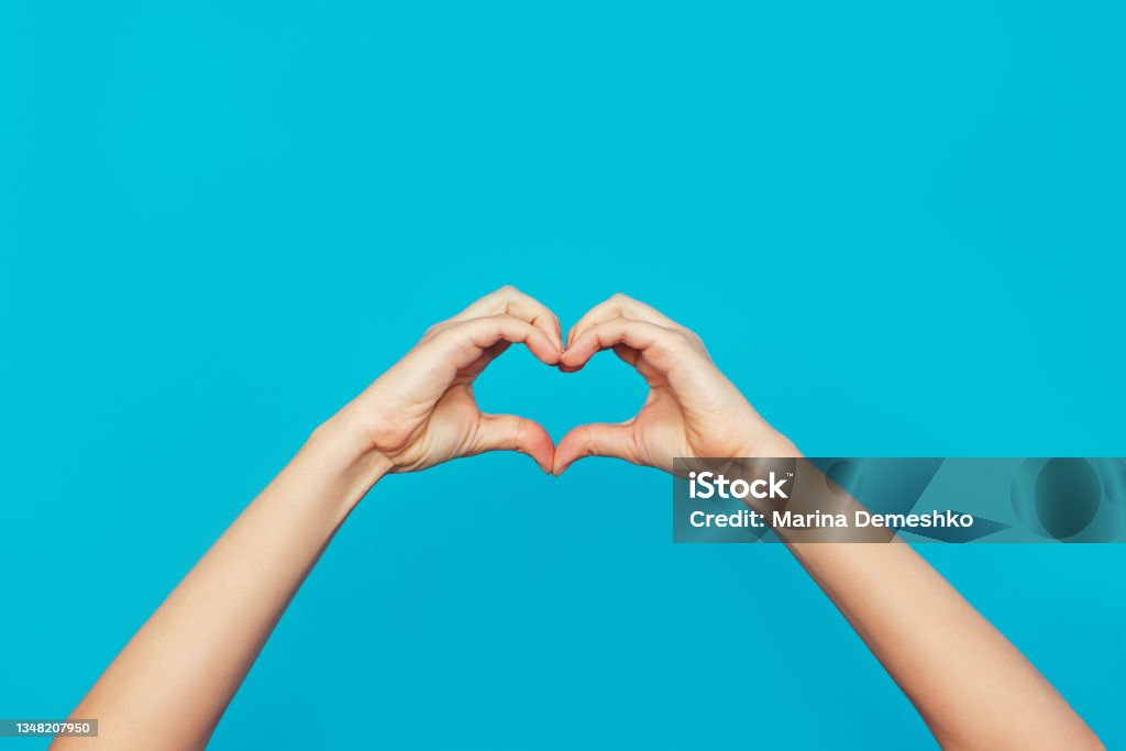 Female hands showing a heart shape isolated on a bright color blue background Female hands showing a heart shape isolated on a bright color blue background. Sign of love, harmony, gratitude, charity. Feelings and emotions concept Gratitude Stock Photo