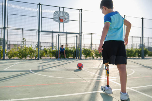 Two friends playing football, one has a leg prosthesis and is kicking a penalty. Two friends playing football, one of them has a leg prosthesis and is kicking a penalty. Kids playing sports together. prosthetic equipment stock pictures, royalty-free photos & images