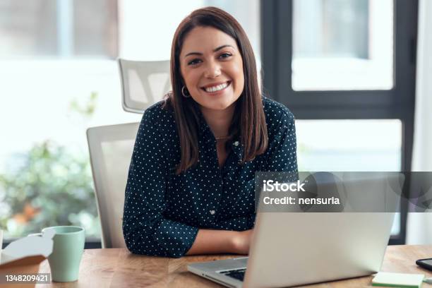 Smiling Business Woman Working With Laptop While Looking At Camera In Modern Startup Office Stock Photo - Download Image Now
