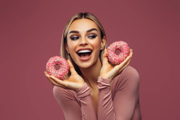istock Young beautiful woman holding pink donuts 1348212309