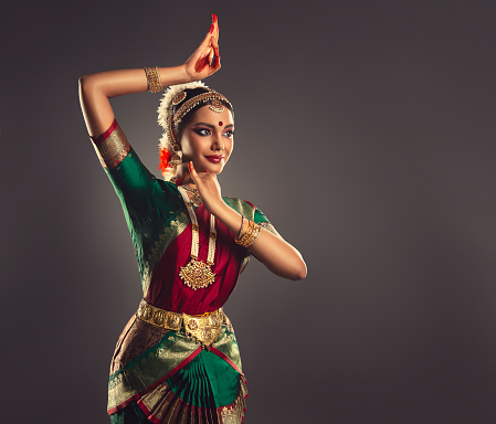 Classic dance indian costume is dressed on attractive woman, who is demonstrating traditional movement of national dance bharatanatyam. Suitable jewelry set on her. Symbolic pose of ancient folk dance. Beauty of classical traditions.