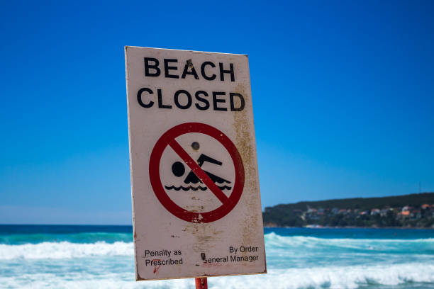 sign reading beach closed with crossed-put swimmer in front of blue ocean in australia - surf rescue imagens e fotografias de stock