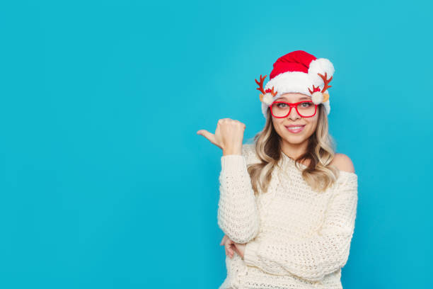istock A young woman in a white warm sweater and a red Santa hat points at empty copy space. Christmas and New Year concept 1348216001