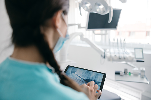 Close up of female dentist looking at dental x-ray on digital tablet at dental clinic
