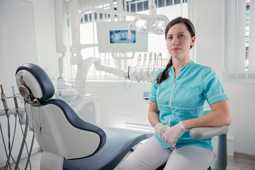 Portrait of young female dentist sitting on chair at dental clinic