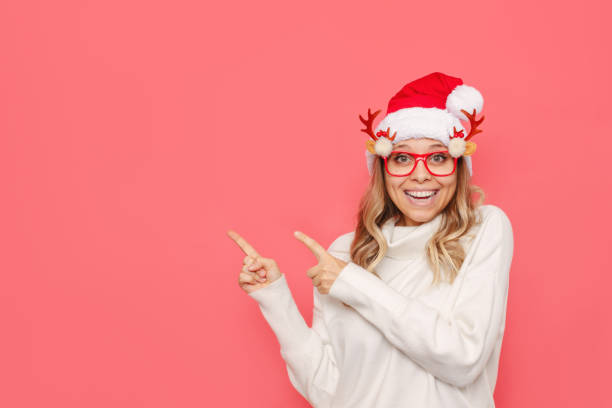 istock A young woman in a white warm sweater and a red Santa hat points at copy space for text or design. Christmas and New Year concept 1348222957