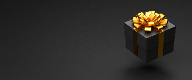 istock A dark present box with golden ribbon and bow hovering over a black stone background. Copy space - web banner size 1348227437