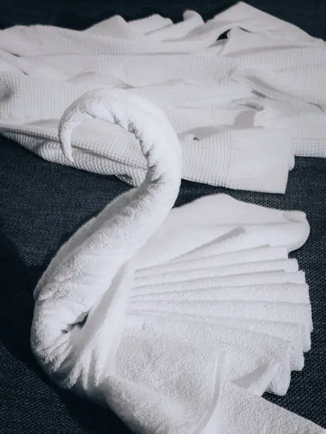 White towels are folded in a swan shape on the hotel bed. Origami - Towel swan.