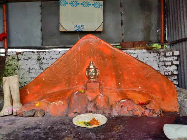 Photo of Stock photo of ancient lord Mhasoba copper face mural installed on orange color painted stone, devotees offering food to god at Kolhapur, Maharashtra, India.