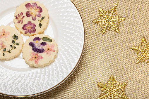 Edible flower cookies with Christmas snowflake ornaments on gold metallic sheet background.