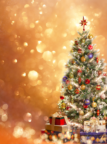 Christmas tree with ornaments and festive gift boxes on golden background with festive bokeh.  New Year or Christmas greeting card