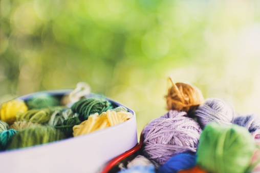 The main object is out of focus. Boxes with knitted multi-colored skeins of yarn on green background nature on sunny days. Bokeh. Background