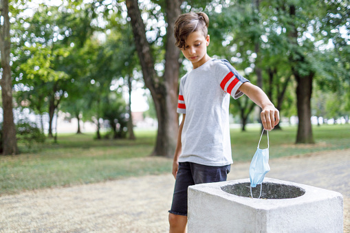 Boy walking in the park and putting protective mask into trash bin