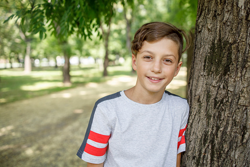 Cheerful young boy leaning onto a tree in a public park