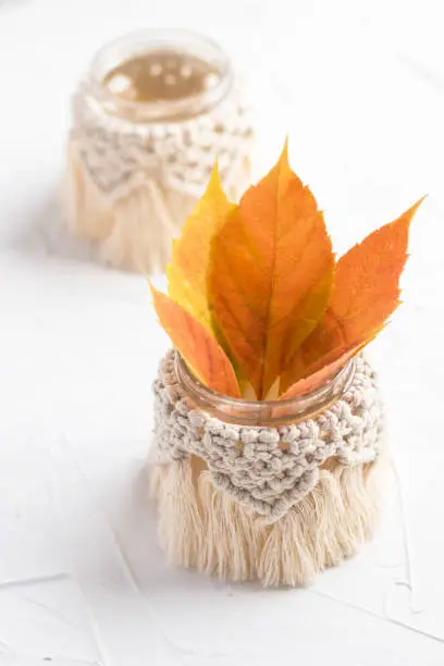 Small glass vases, jars, candleholders with macrame cover. Beautiful yellow-orange autumn leaves. Boho style. Bohemian home decor. Wedding accessory.