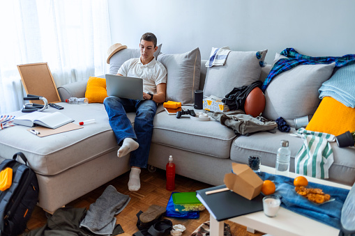 Serious Male Teenager using laptop in his messy room during the day