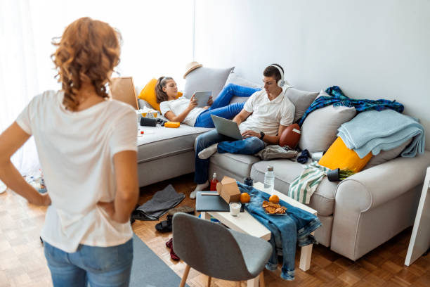 istock Overworked mother looking at brother and sister spending time using laptop and digital tablet in messy living room. 1348239230