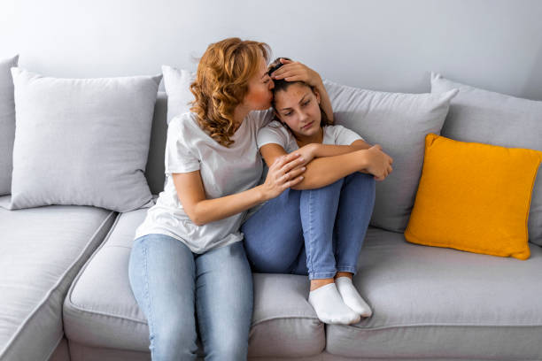 Caring mother calming and hugging upset little daughter Mother Talking With Unhappy Teenage Daughter On Sofa emotional support stock pictures, royalty-free photos & images