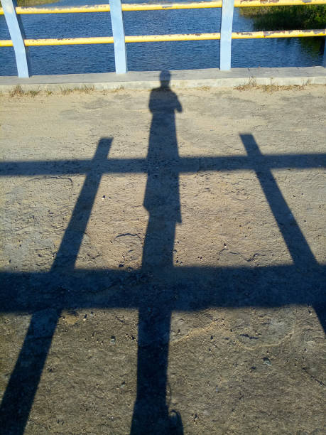 淡い未舗装道路上の男の影または輪郭。橋の手すりを持つ男の影 - single line yellow road asphalt ストックフォトと画像