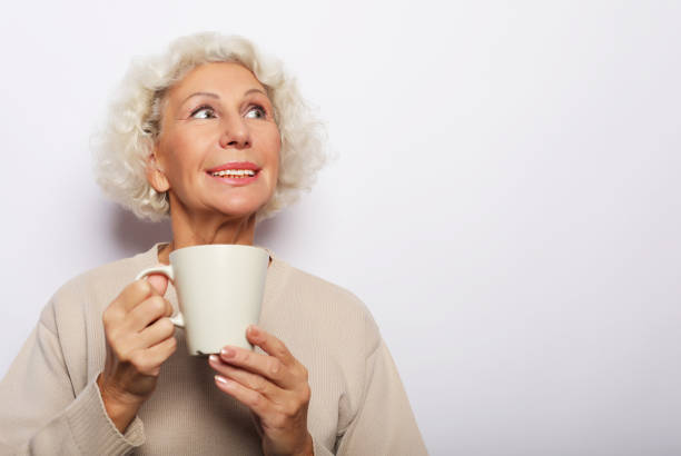 istock old excited lady smiling laughing, holding cup drinking coffee, tea, beverage on grey background 1348242765