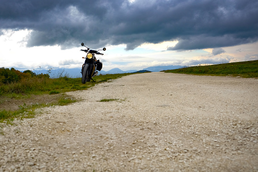 A motorcycle parked on the side of a country road under a cloudy sky