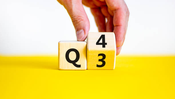 From 3rd to 4th quarter symbol. Businessman turns a wooden cube and changes words 'Q3' to 'Q4'. Beautiful yellow table, white background. Business, happy 4th quarter Q4 concept, copy space. stock photo