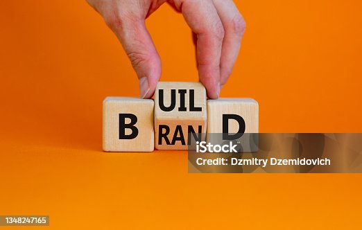 istock Build your brand symbol. Businessman turns wooden cubes and changes the word 'build' to 'brand'. Beautiful orange background. Build your brand and business concept. Copy space. 1348247165