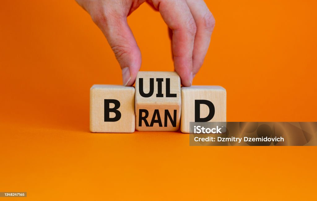 Build your brand symbol. Businessman turns wooden cubes and changes the word 'build' to 'brand'. Beautiful orange background. Build your brand and business concept. Copy space. Advertisement Stock Photo