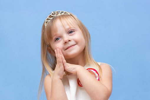 Funny little princess girl in silver crown and pink dress over blue background