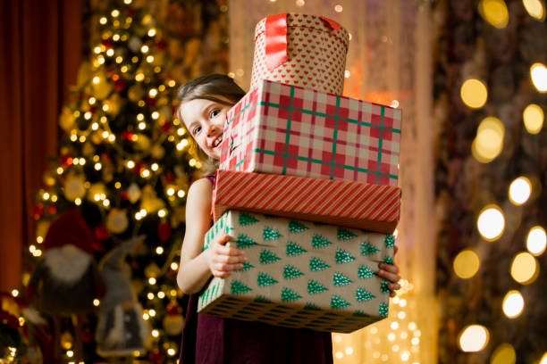 Excited curious little girl smiling, holding a pile of Christmas gifts stock photo